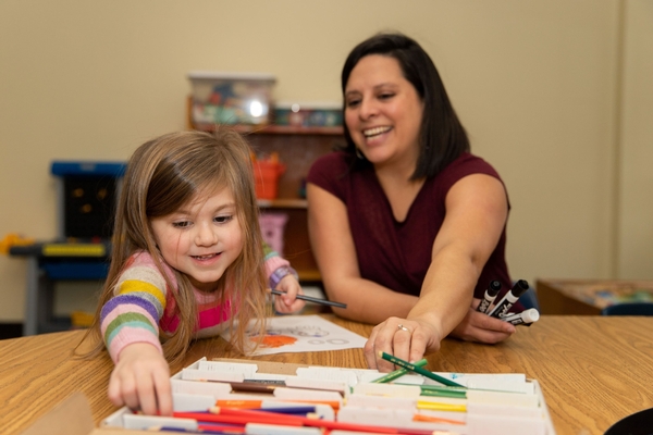 A preschool teacher colors with a student